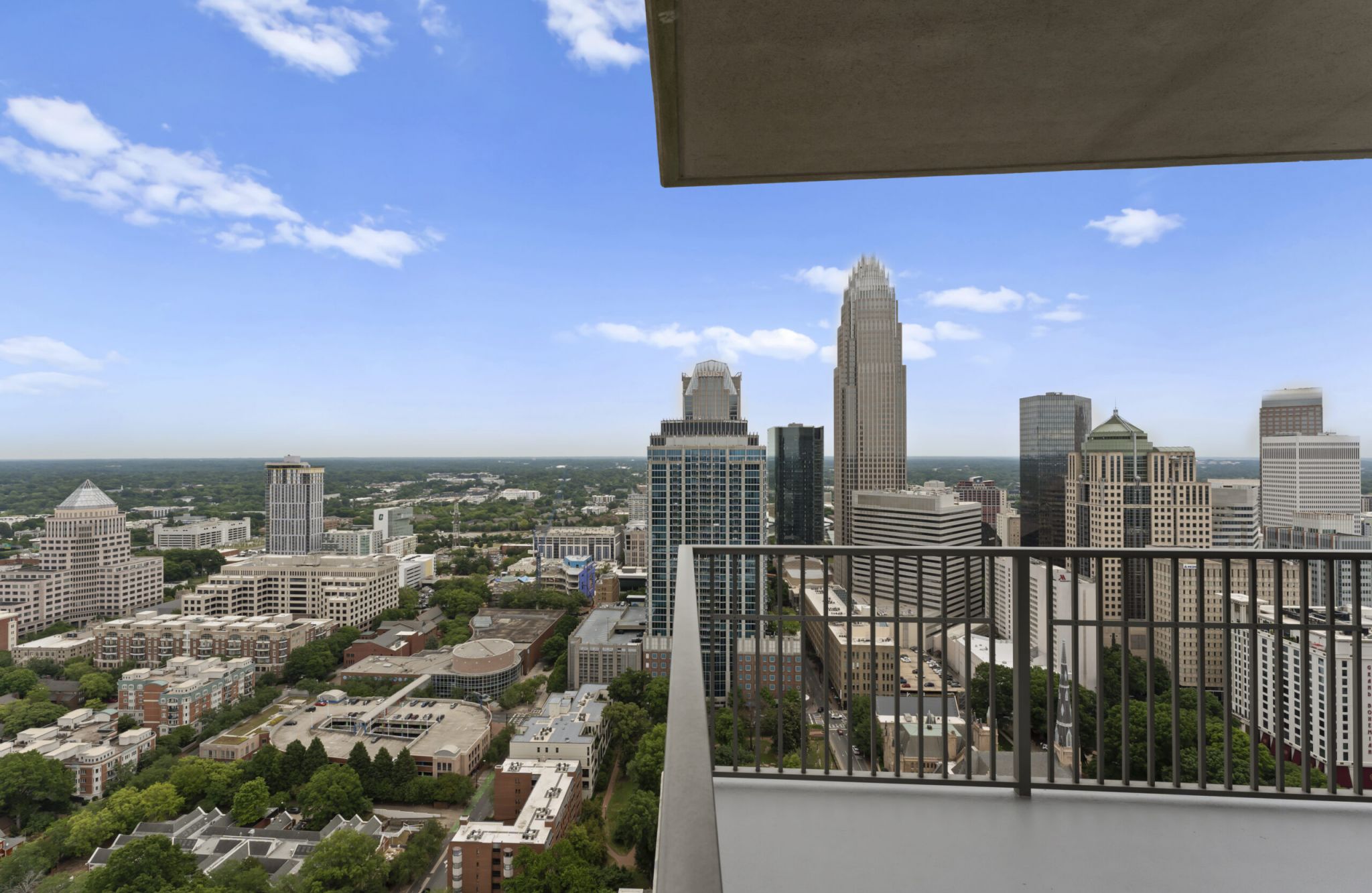 Woman holding balcony railing at The Vue Charlotte apartments while looking out at birds-eye view of the city