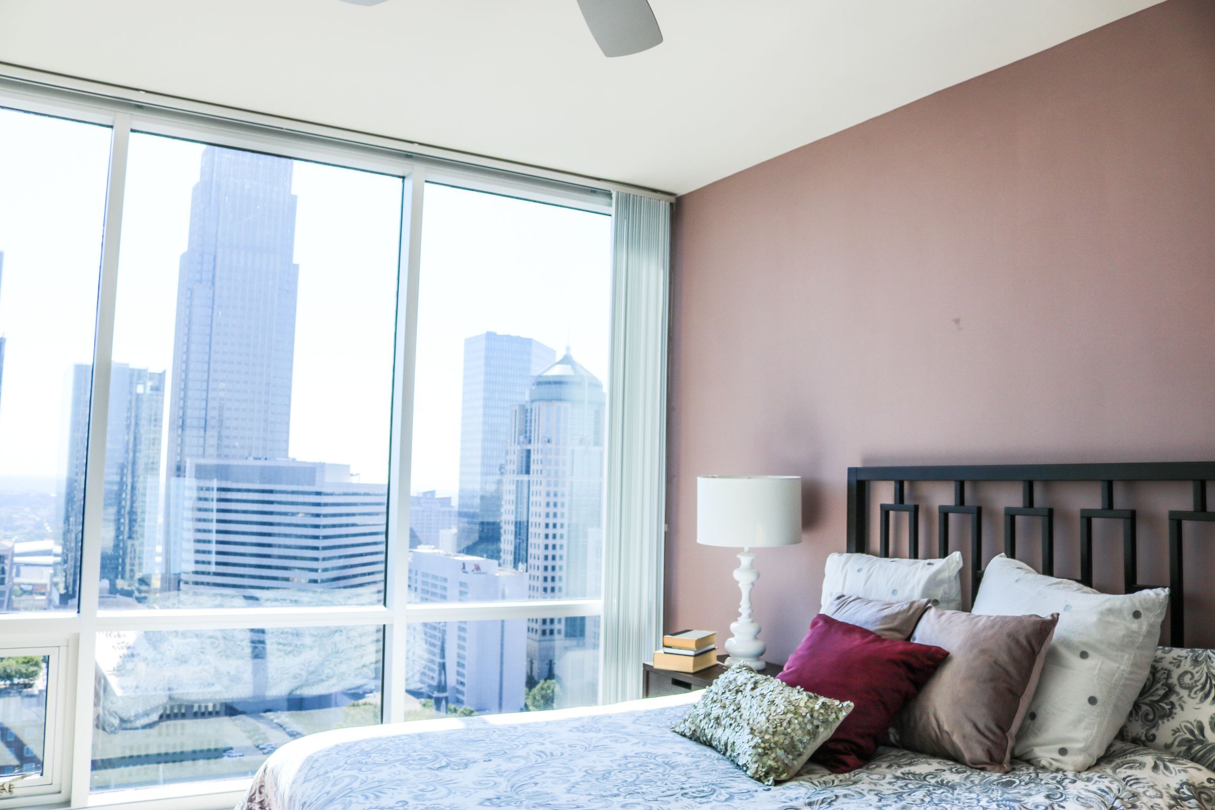 The Vue at Charlotte apartment interior bedroom with a large bed, a chair, and a view of Uptown Charlotte through floor to ceiling windows